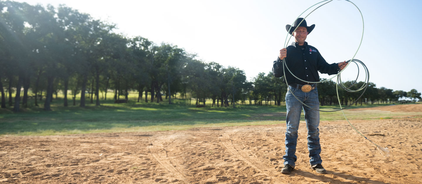 Haven Meged standing in an arena, holding a rope wearing a black shirt and black cowboy hat.